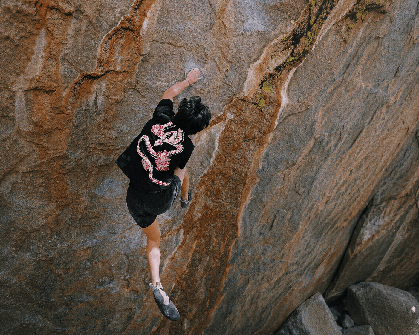 A person in a black shirt with a red snake design rock climbing on a textured rock face.