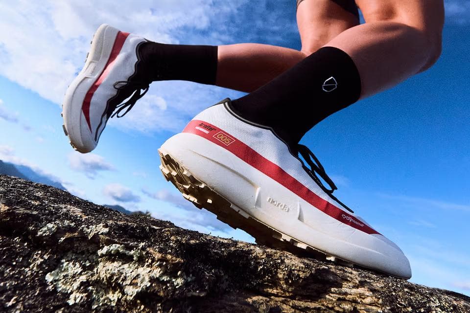 Feet in white and red trail running shoes stepping on rocky terrain under a blue sky.