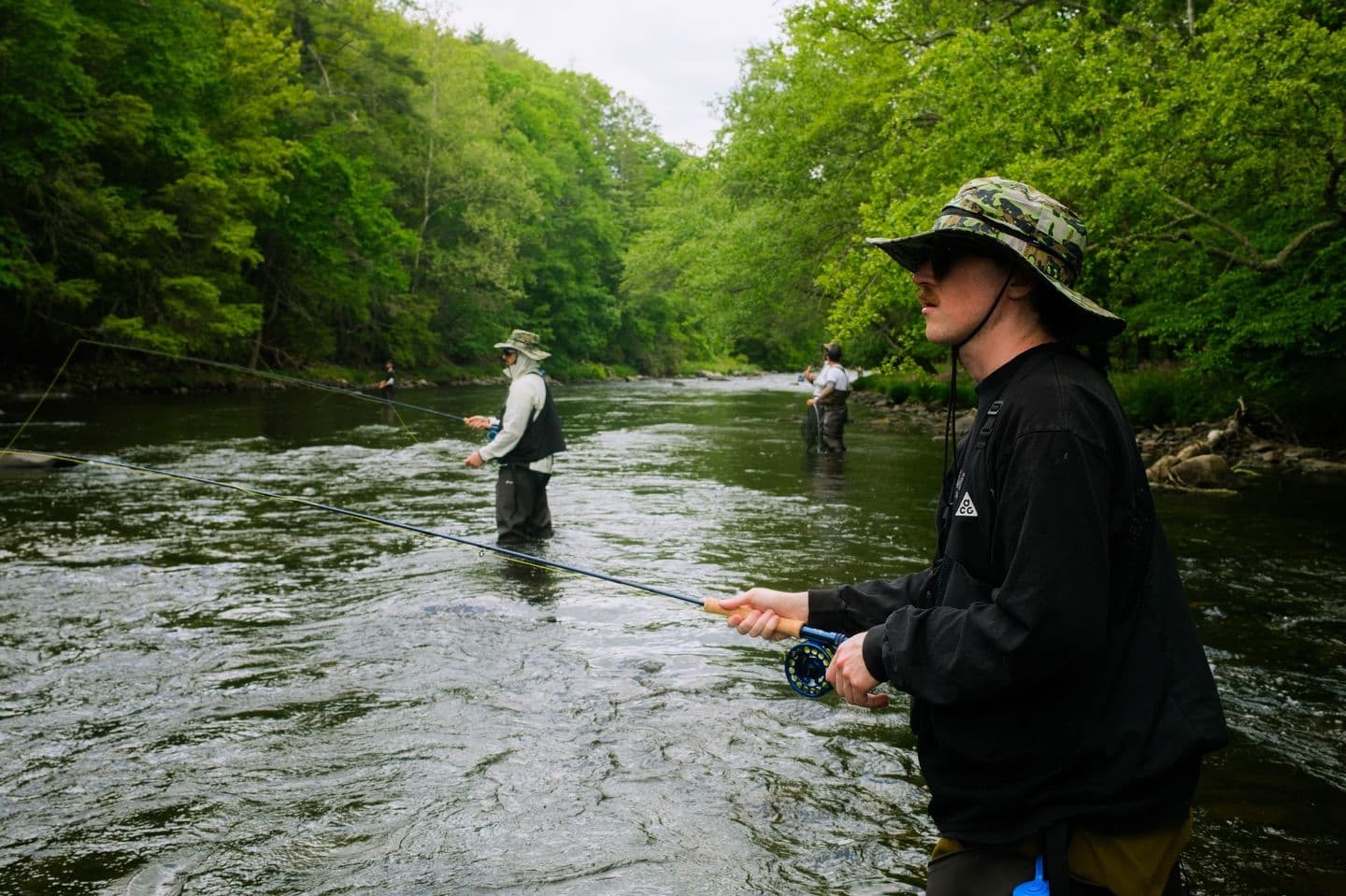 People fly fishing in a flowing river surrounded by lush green forest.