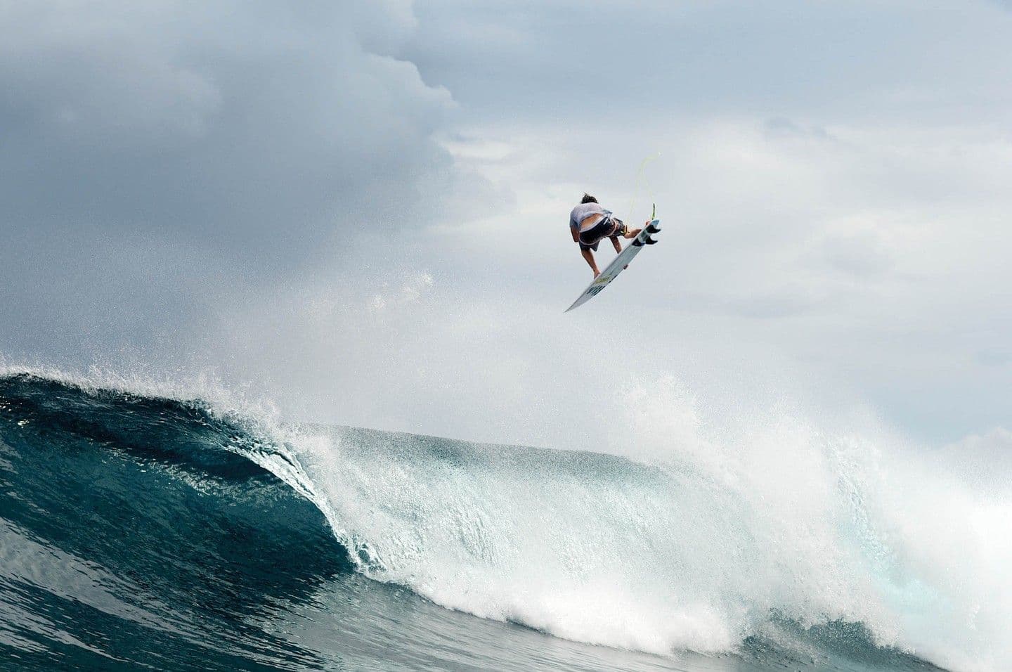 A surfer is airborne above a large breaking wave.