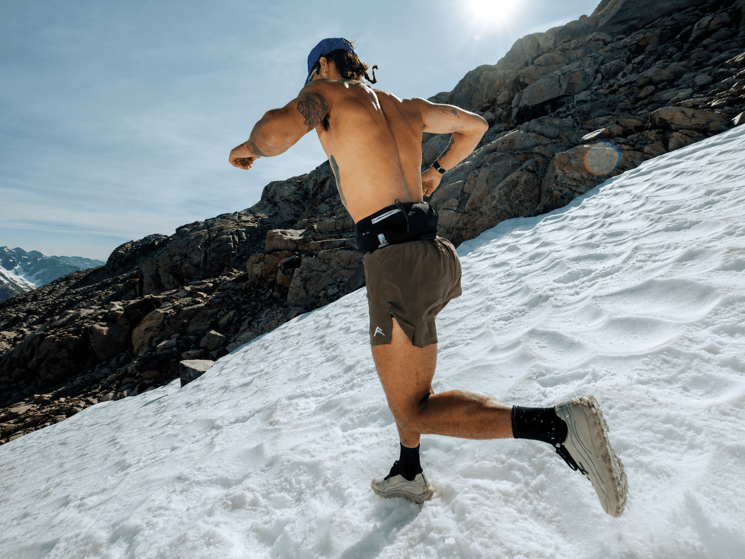 Shirtless runner ascending a snowy mountain slope.